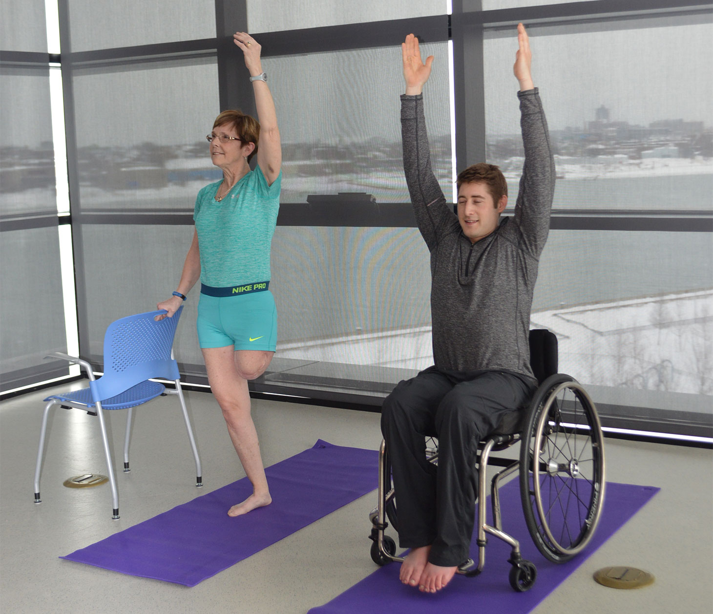 A woman with an amputated leg and a young man in a wheelchair do yoga.