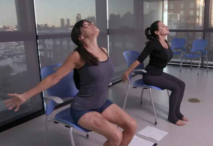 Two women do adaptive yoga while seated in chairs.