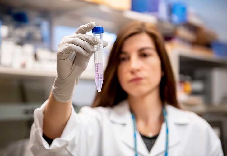 A female lab tech holds up a vial half-full of a clear liquid.