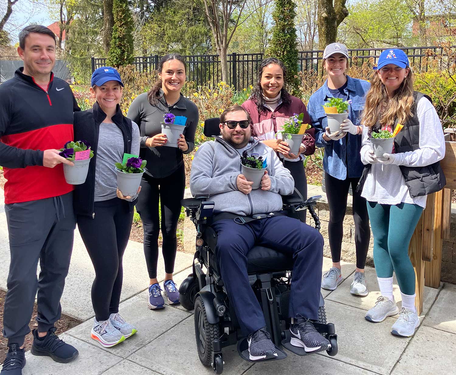 Smiling young people in outdoors gear holding small potted plants.