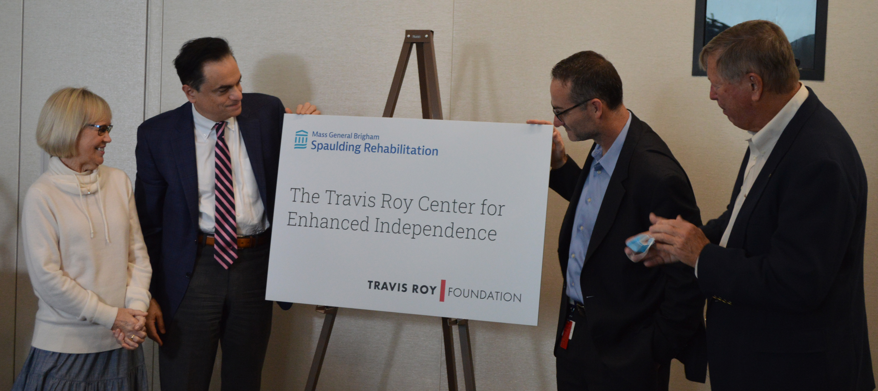 Four people looking at a sign that says "The Travis Roy Center for Enhanced Independence"