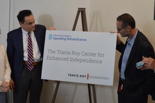 two people looking at a sign that says "The Travis Roy Center for Enhanced Independence"