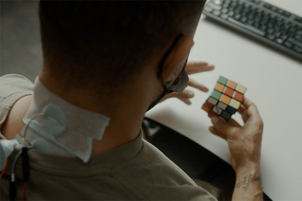 A man with electrodes taped over his spine does a Rubiks Cube.