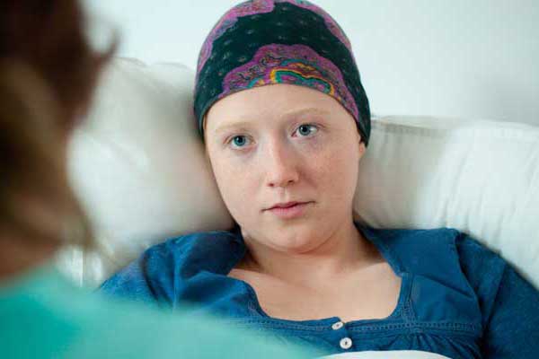 A teen girl with a cancer headwrap in a hospital bed.