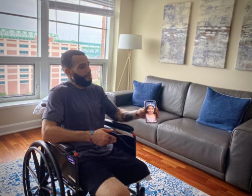 Chris in his wheelchair in his living room, holding up a photo of his daughter on his phone.