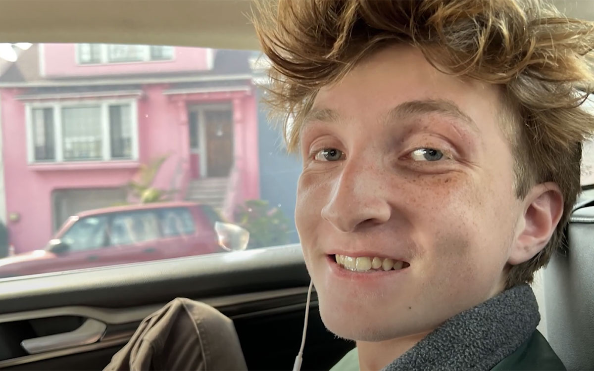 A teenaged boy with tousled red hair in the passenger seat of a car.