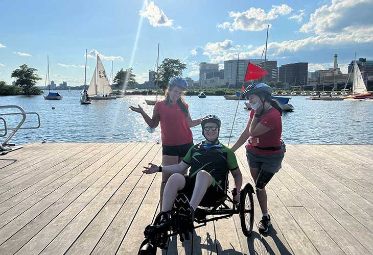 Jake at the Boston waterfront on a reclining bicycle, flanked by two standing fellow patients.