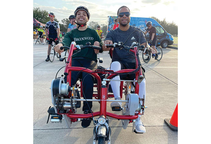 Joshua and his brother, two young Black men, on an adaptive bicycle for two.