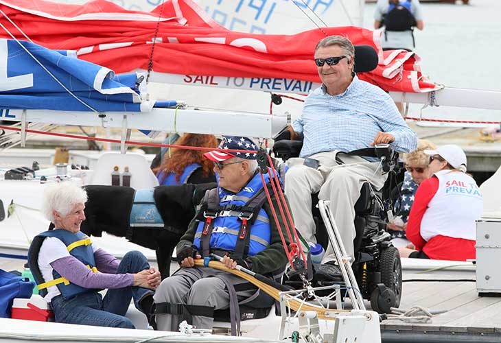 Paul on the dock in his wheelchair with two of the participants in his Sail To Prevail program.