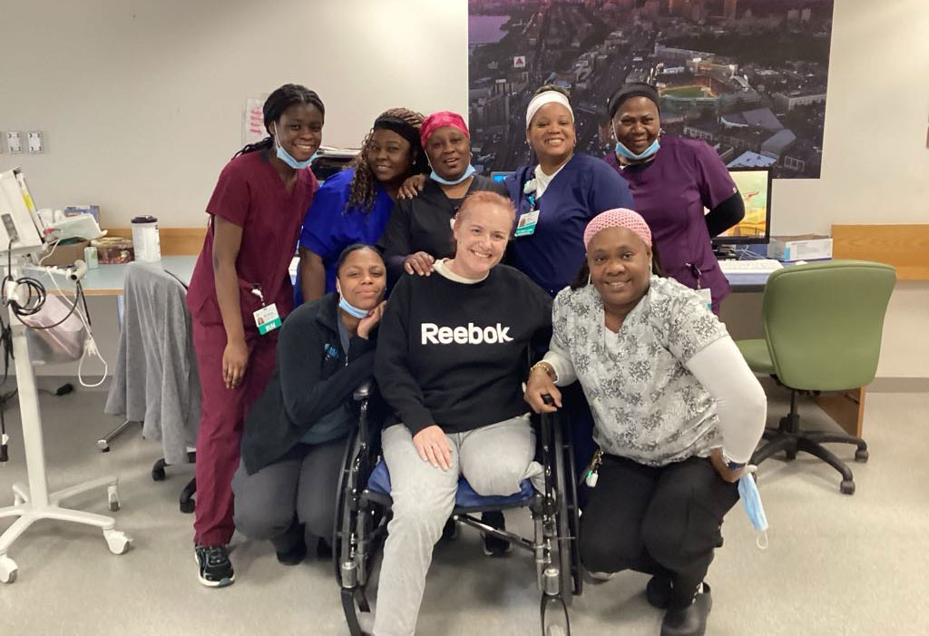 A grinning woman in a wheelchair, surrounded by smiling medical staff.