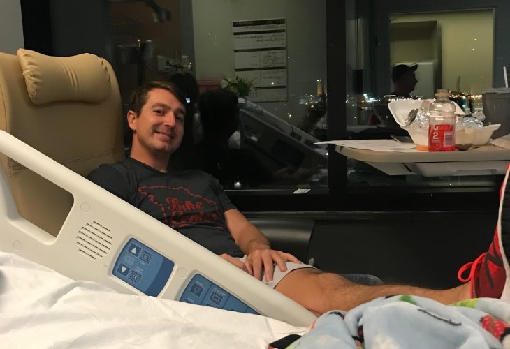 Tim looking cheerful  in a chair beside his hospital bed.