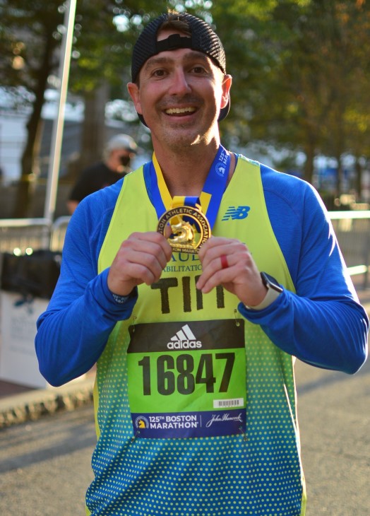 Tim in running gear, proudly holding up a gold medal.