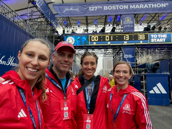 Four program members in red marathon jackets and medical name tags, posing at an entrance to the 127th Boston Marathon.