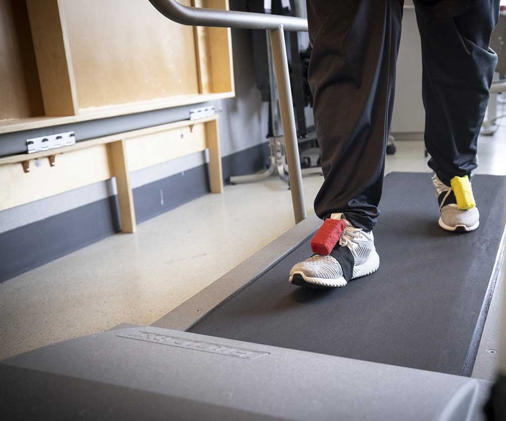 A patient walking on a treadmill with weights on his feet.