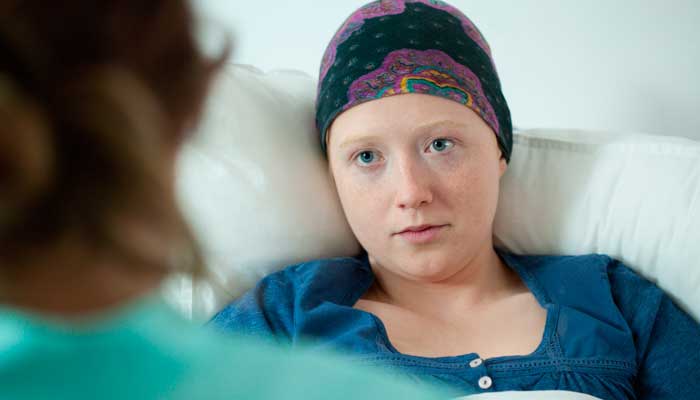 A teen girl with a cancer headwrap in a hospital bed.