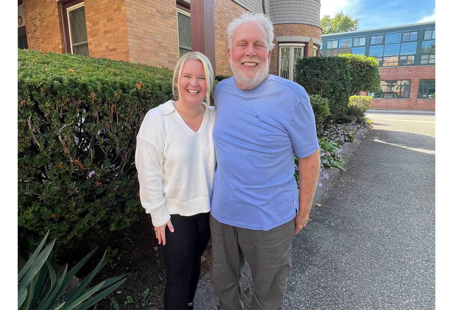 Brad, a bearded older man, and his daughter Catie pose in front of a building in Cambridge.